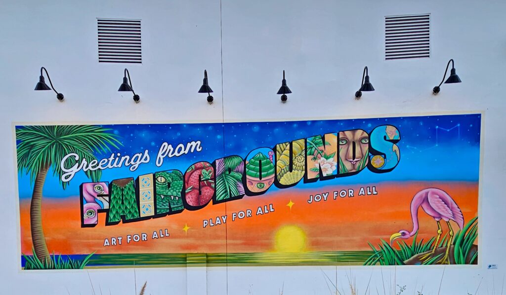 A postcard style mural that says greetings from fairgrounds on the exterior of Fairgrounds St. Pete