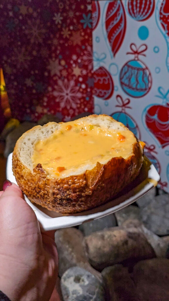 a hand holding a place with a large sourdough bread bowl filled with North Pole Newberg soup