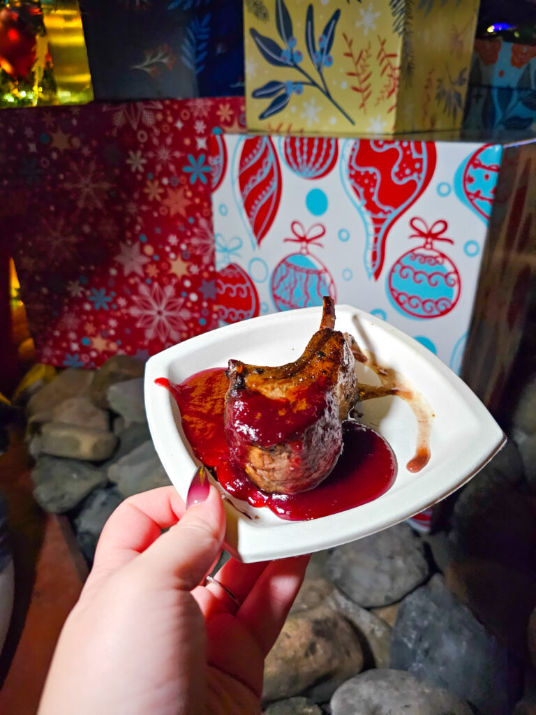 a hand holding a plate with two lamb chop ribs covered in a cranberry and peppered apple relish