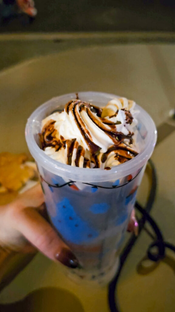 a hand holding an insulated cup with frozen hot chocolate in it covered in whipped cream and chocolate.