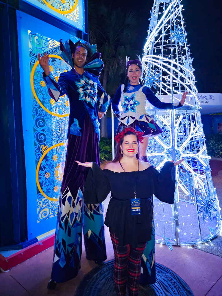 kristin standing in front of two seaworld orlando employees that are on stilts and dressed in holiday gear