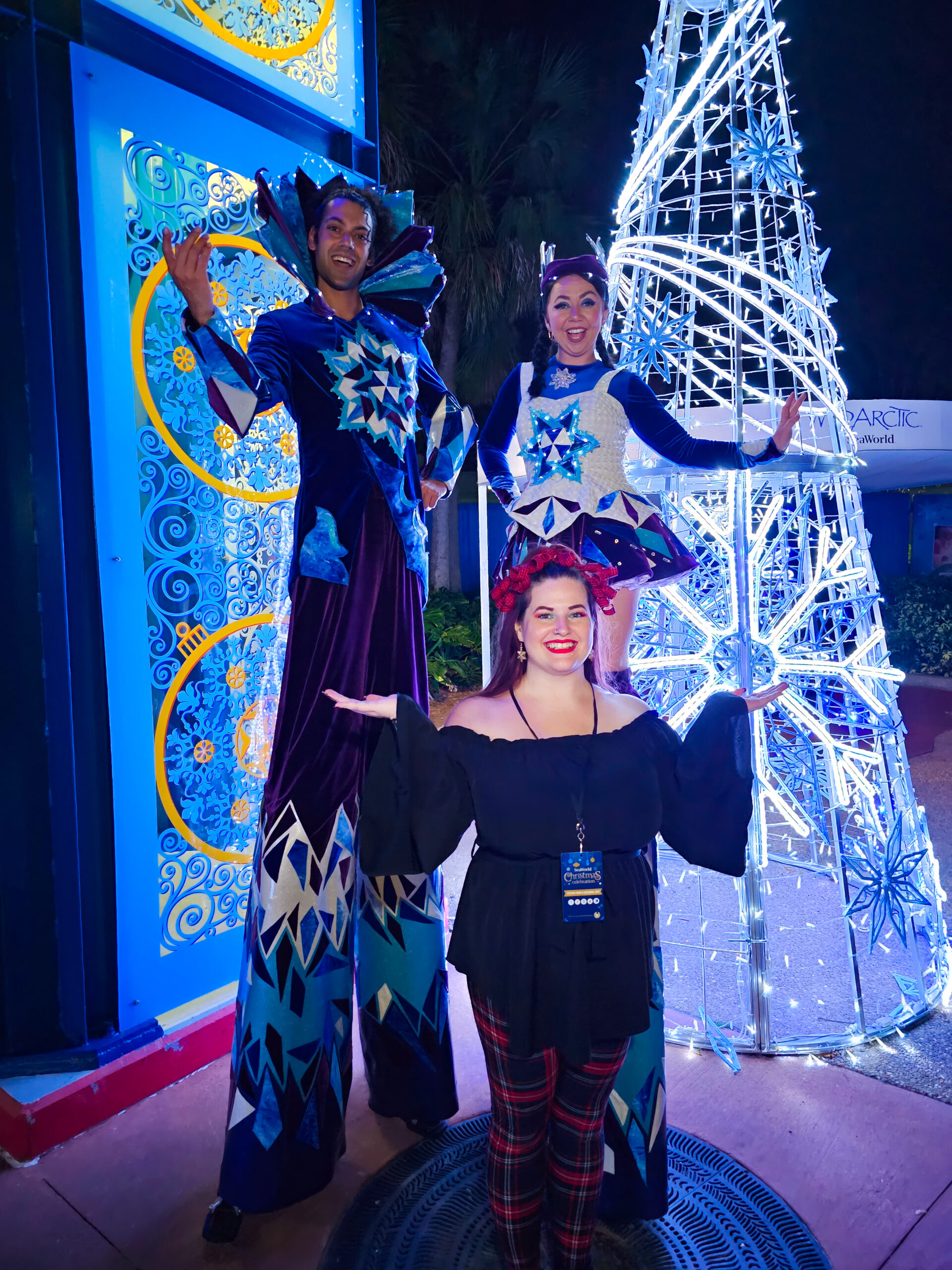 Kristin standing in front of two SeaWorld Employees on stilts wearing holiday gear.